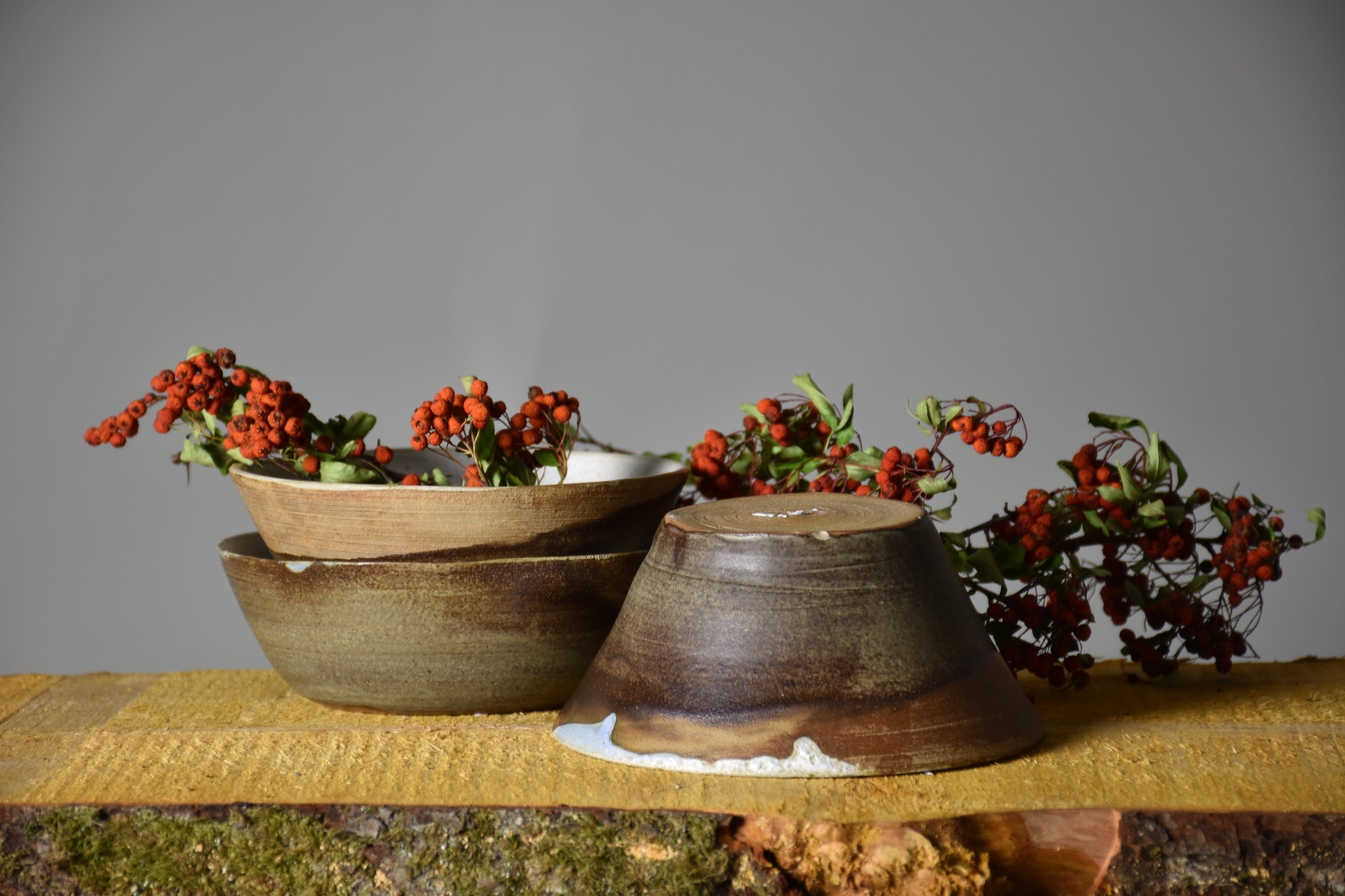 a brown ceramic bowl set on a wooden table, with some rowanberries next to it